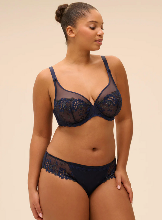 Woman wearing a navy blue lace bra and panties set on a beige background
