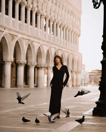 Woman in a black dress standing in front of an architectural structure with pigeons around her.