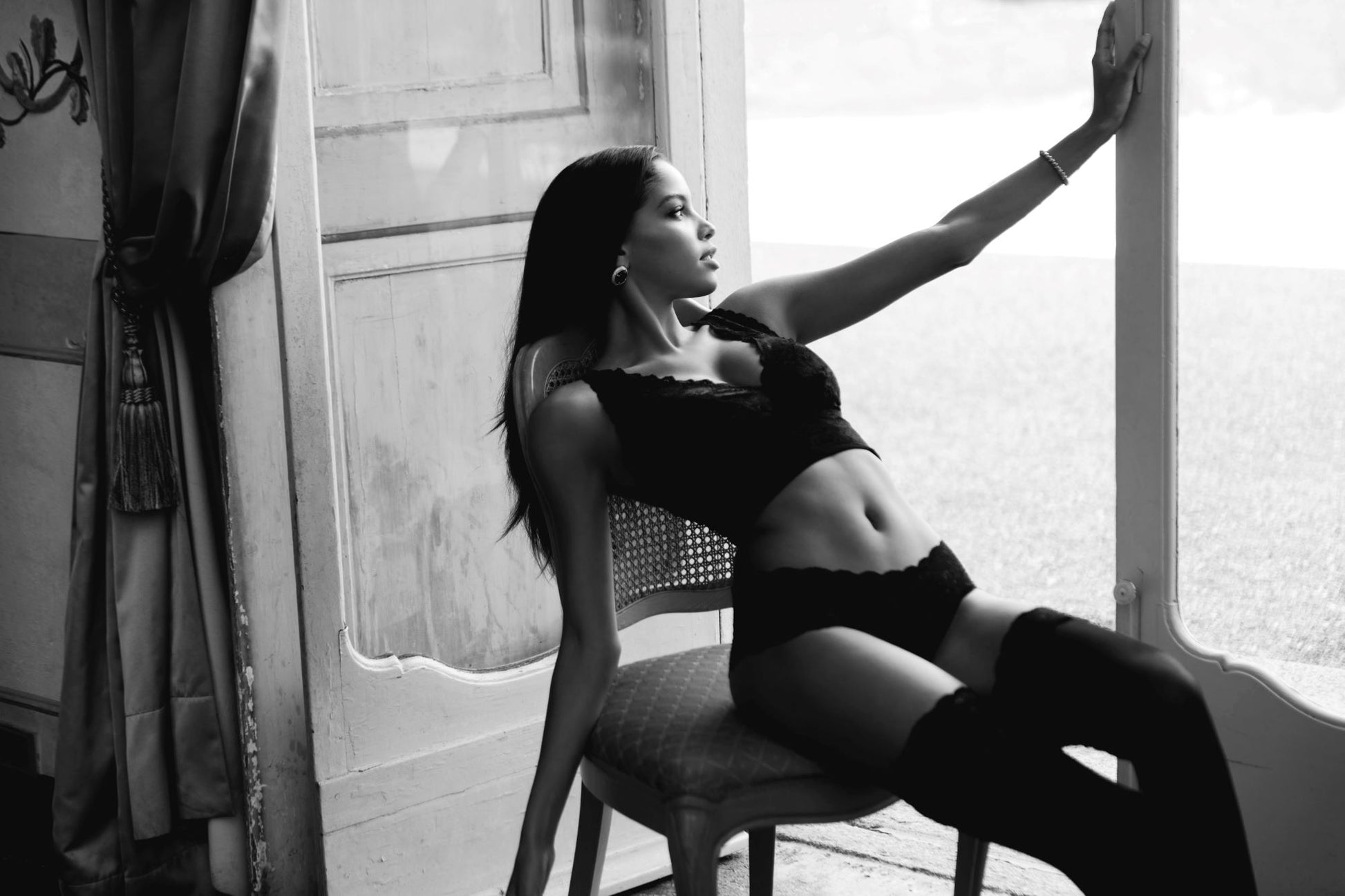 Black and white photo of a woman sitting on a chair by a window