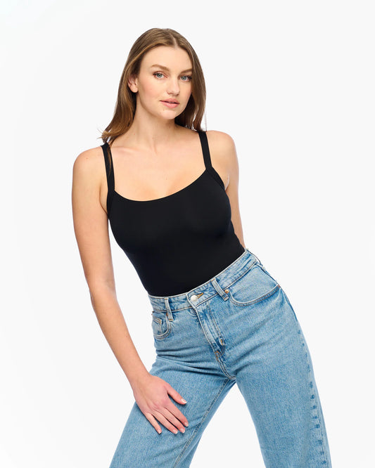 Woman wearing a black tank top and blue jeans on a white background