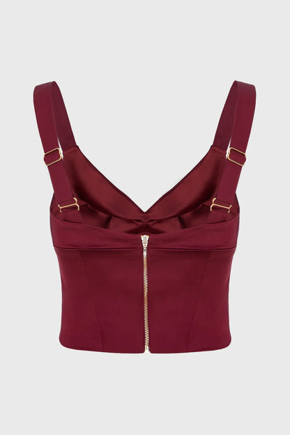 Maroon corset top with gold straps and zipper on a light gray background