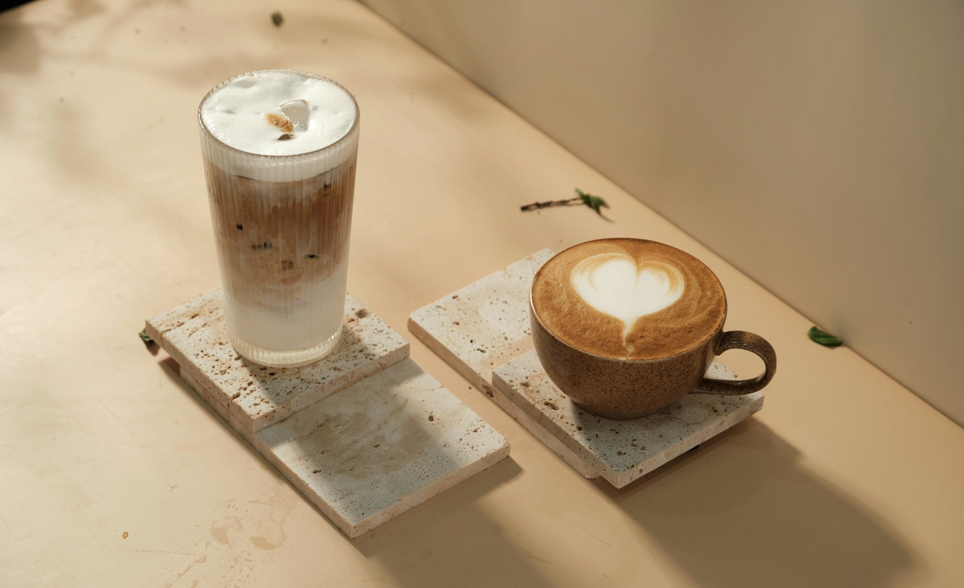Two glasses of coffee on stone coasters on a wooden surface.