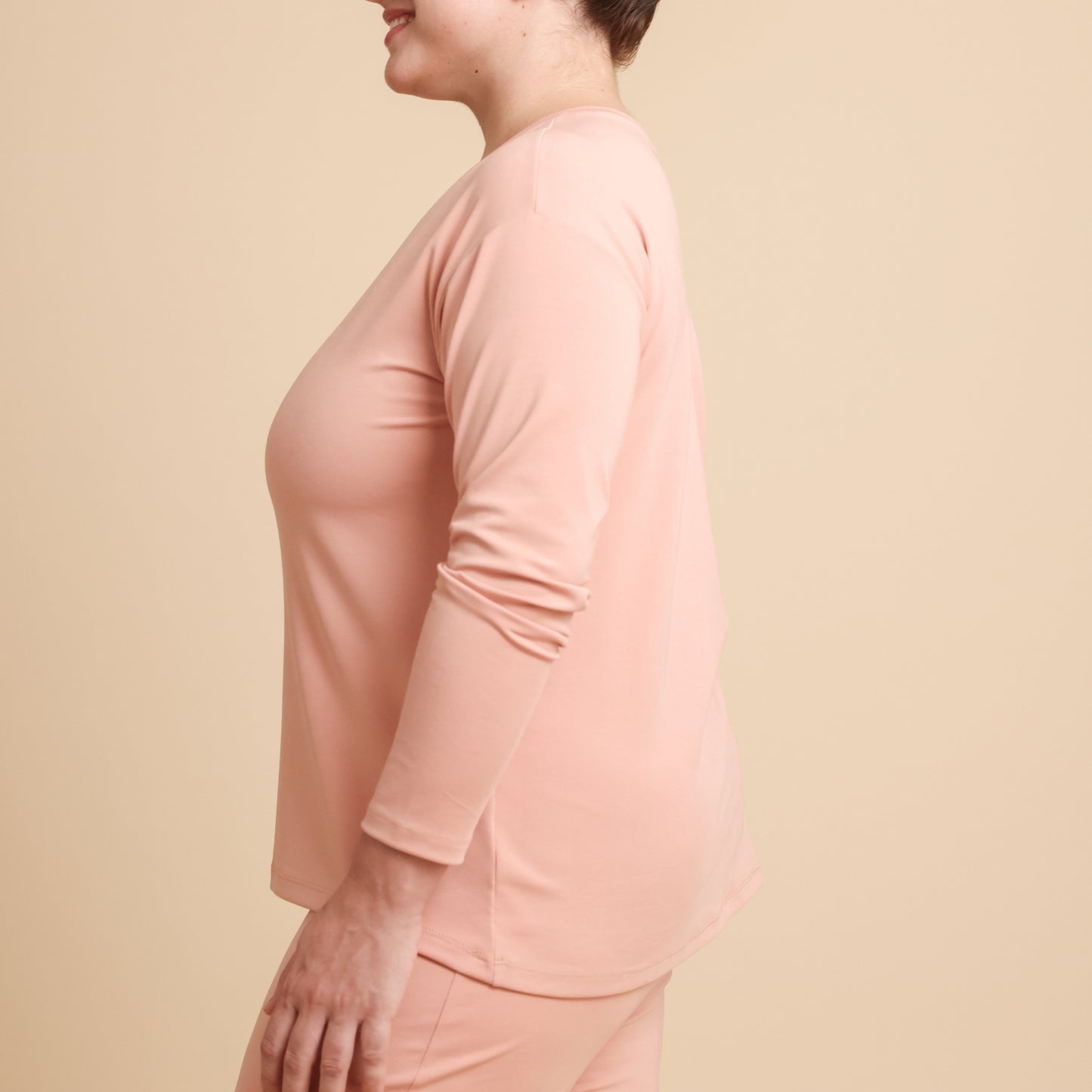 Person wearing a light pink long-sleeve top against a beige background