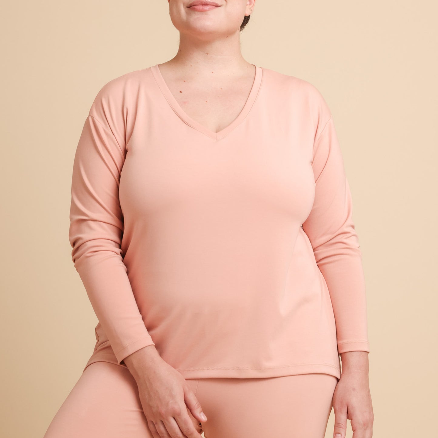 Person wearing a pink long-sleeve top and pants on a beige background