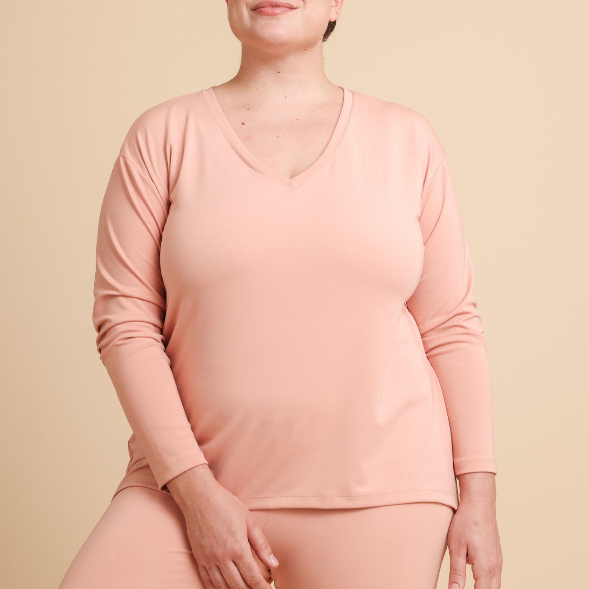 Person wearing a pink long-sleeve top and pants on a beige background