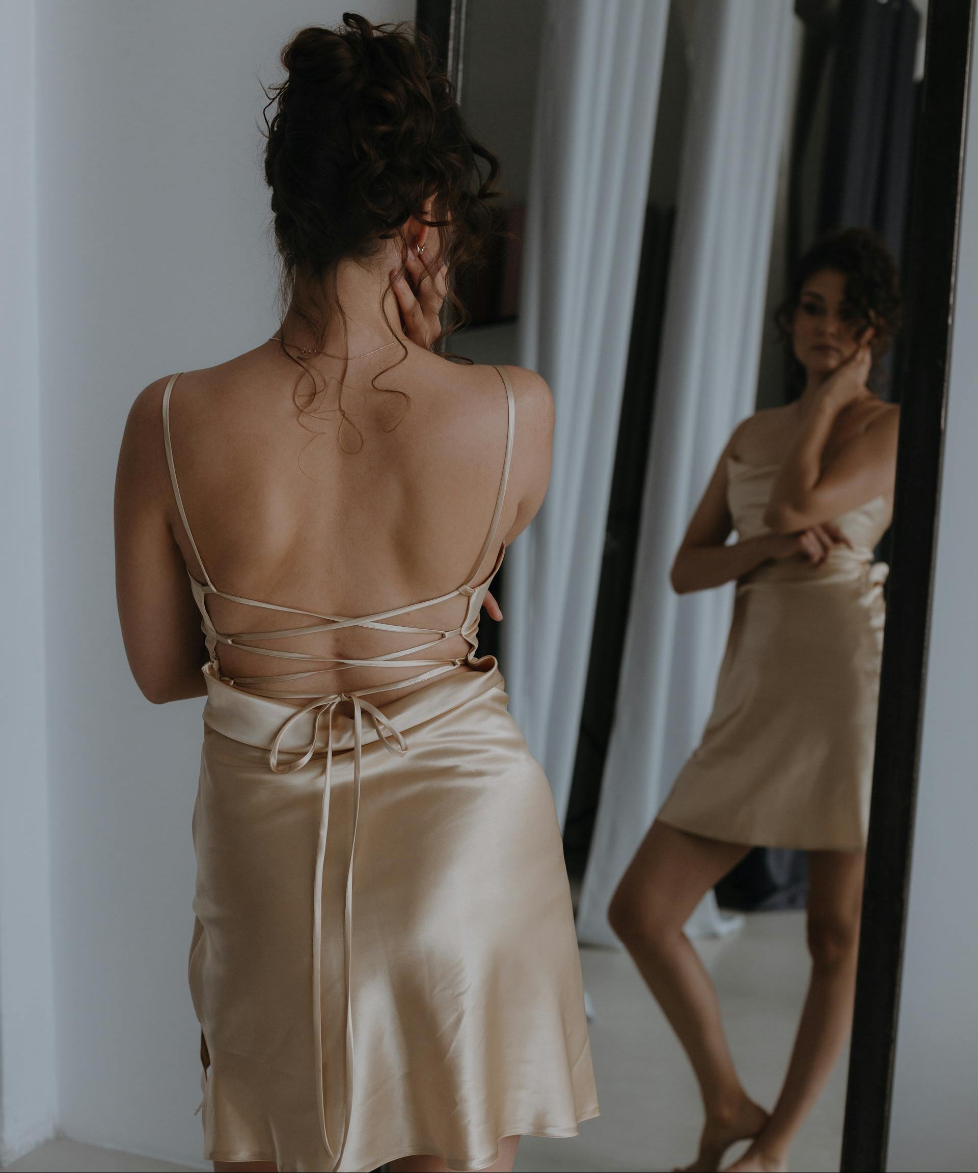 Woman in a beige satin nightgown standing in front of a mirror.