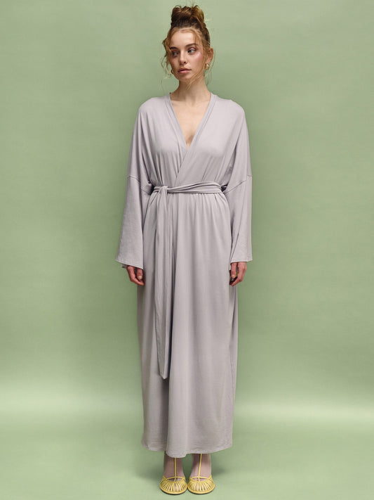 Woman wearing a long light gray dress against a green background