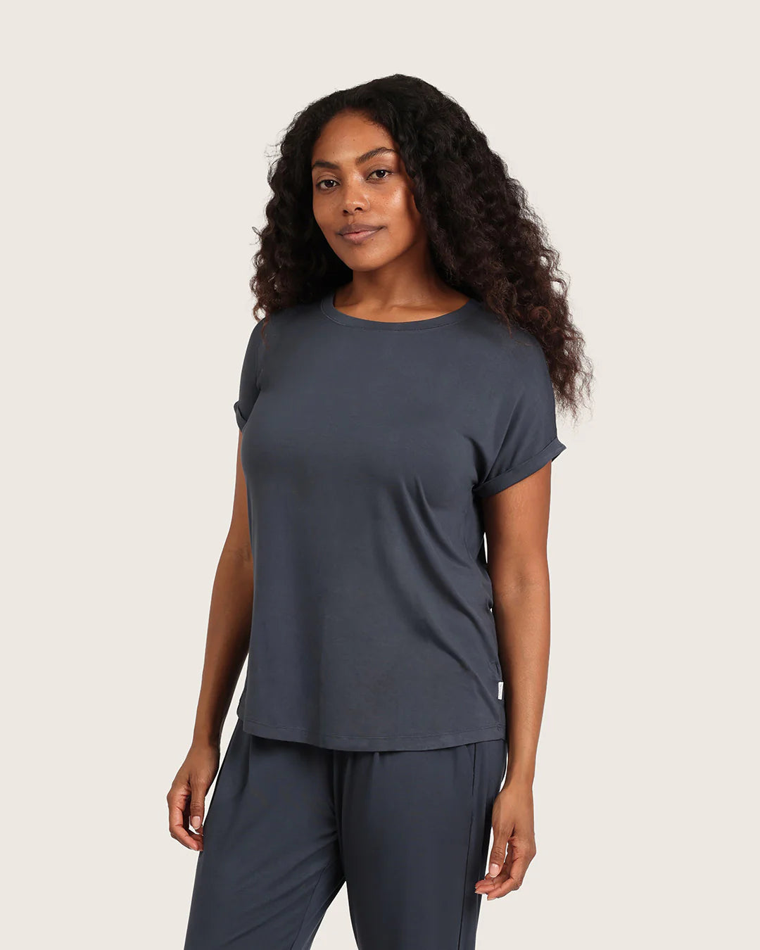 Woman wearing a dark gray t-shirt and pants on a beige background
