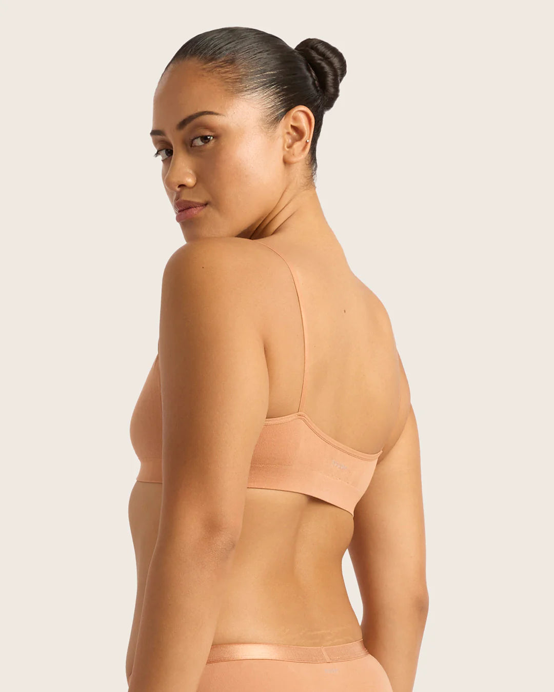 Woman wearing a beige bra and underwear set against a plain background