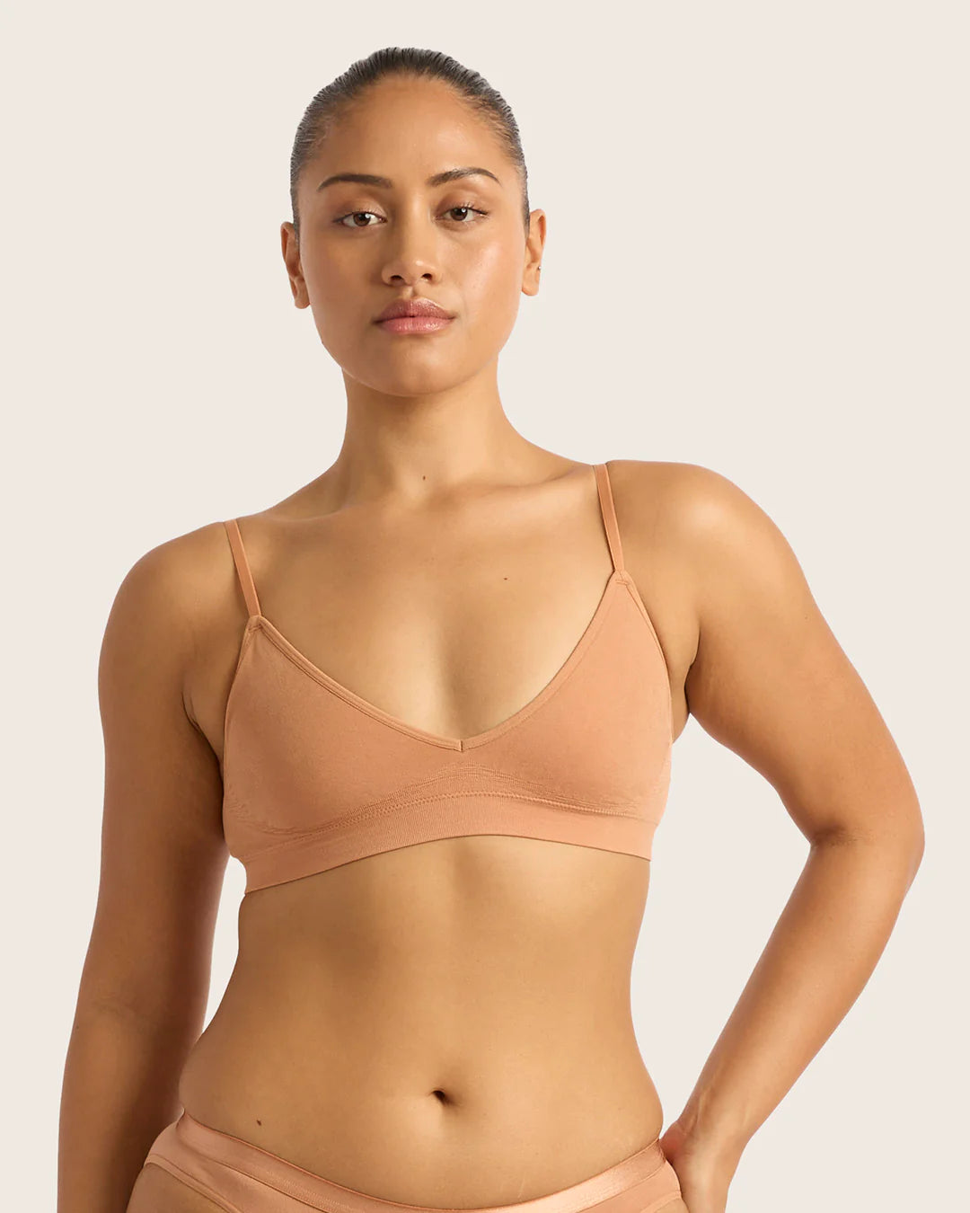 Woman wearing a beige sports bra and underwear set on a light pink background