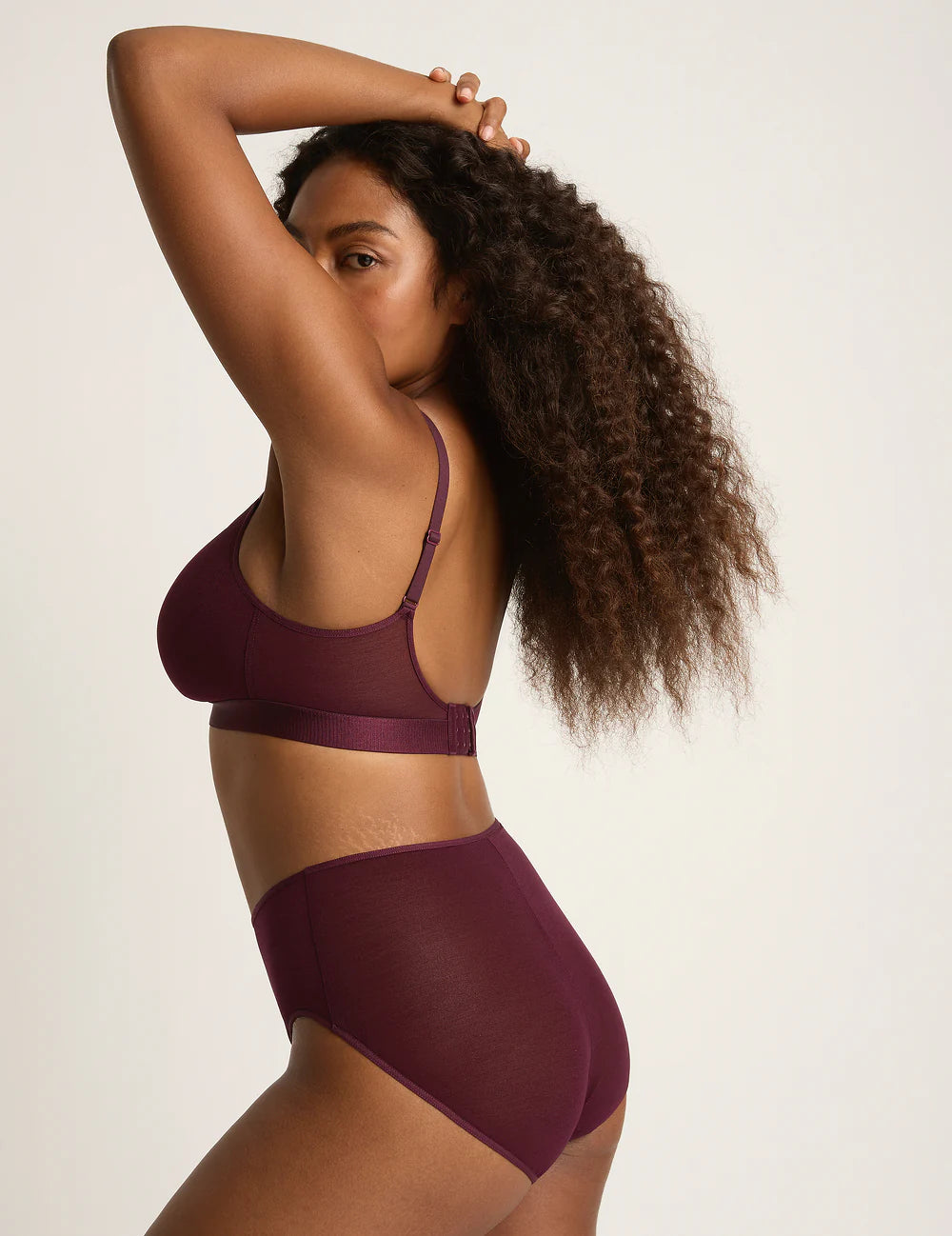 Woman wearing a burgundy bra and underwear set on a plain background