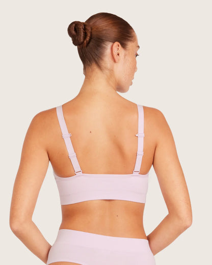 Woman wearing a light purple sports bra and shorts on a plain background