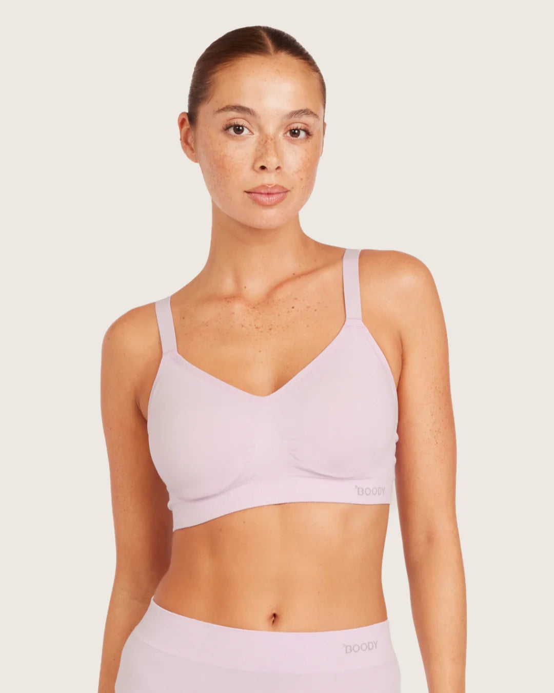 Woman wearing a light purple sports bra and leggings on a plain background
