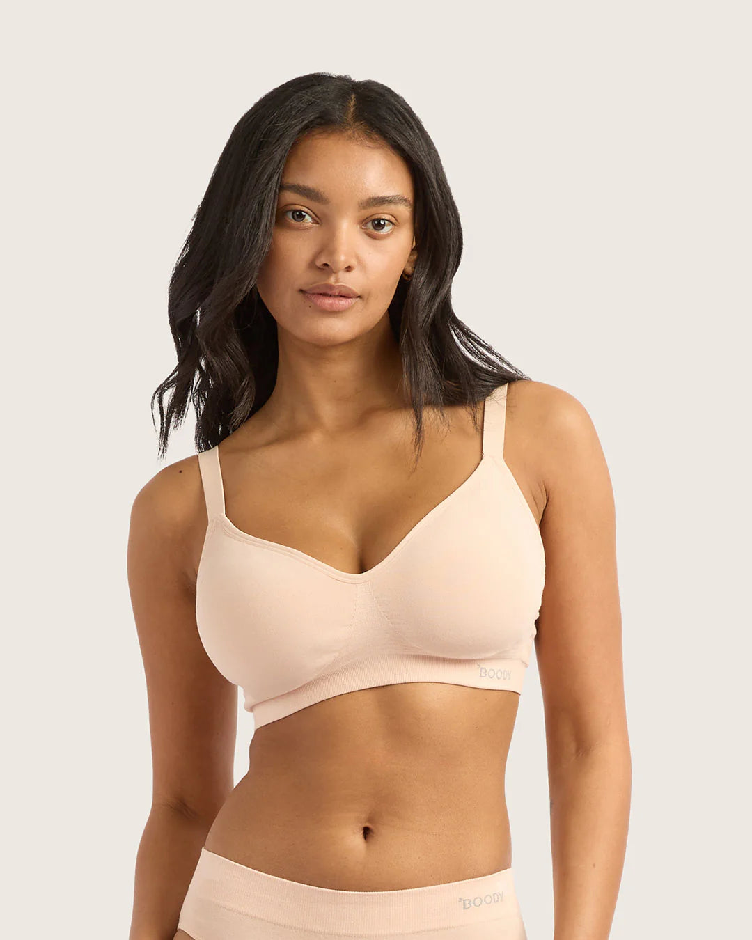 Woman wearing a beige bralette against a plain background