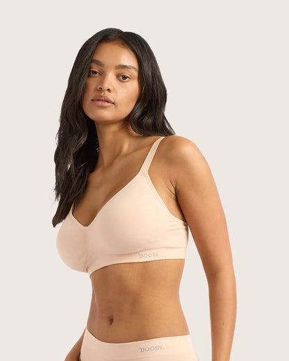 Woman wearing a beige bralette with a plain background