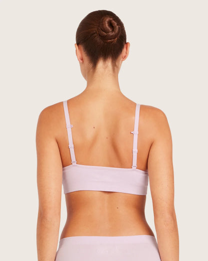 Woman wearing a light purple sports bra and shorts on a plain background