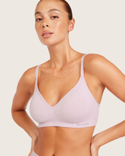 Woman wearing a light purple bralette on a plain background