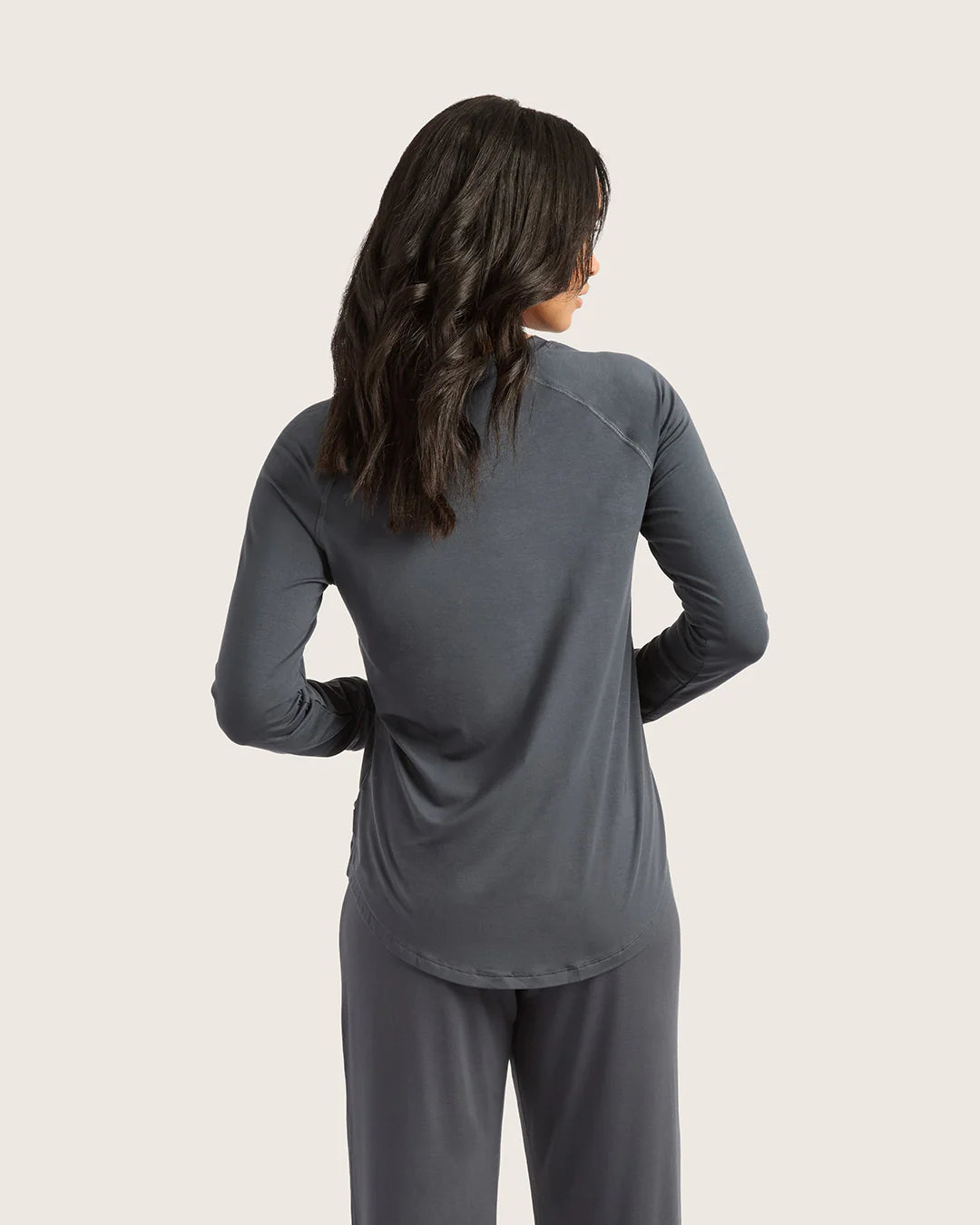 Woman wearing a gray long-sleeve top and pants on a light beige background