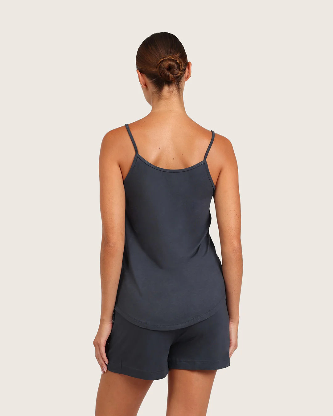 Woman wearing a dark gray tank top and shorts on a light beige background