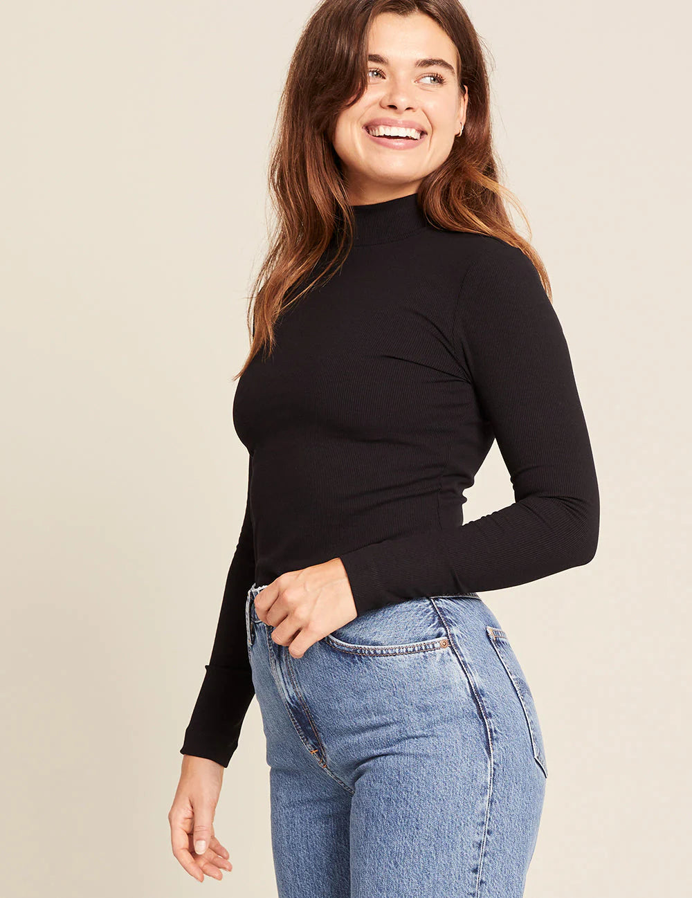 Woman wearing a black long-sleeve top and blue jeans on a beige background