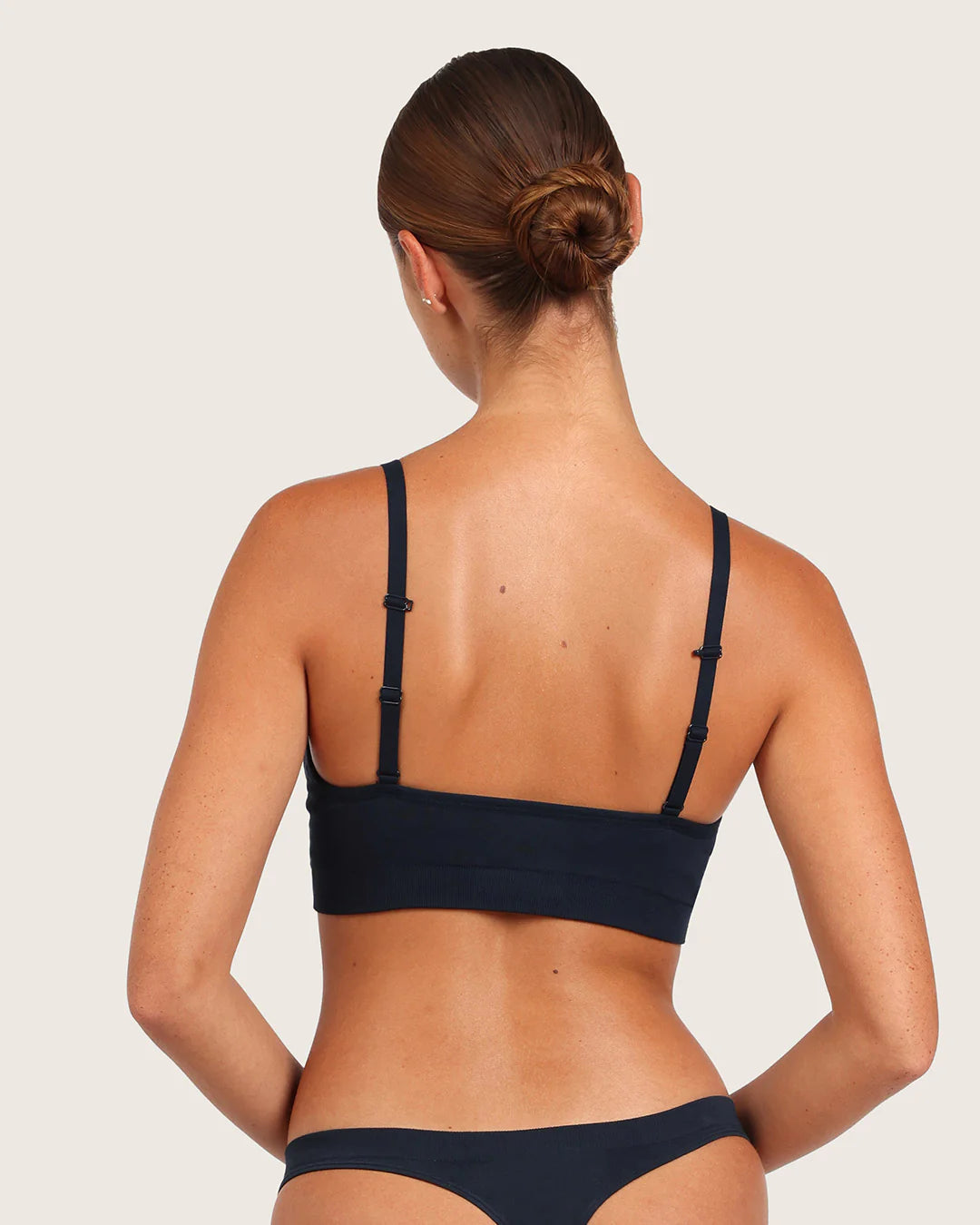 Woman wearing a navy blue bikini set on a light gray background