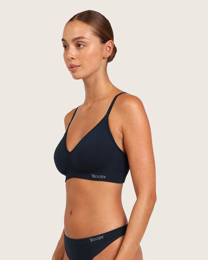 Woman wearing a navy blue bikini with 'Boody' branding on a beige background
