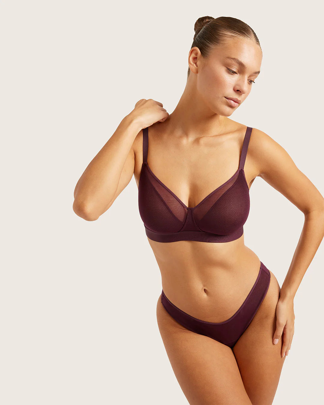 Woman wearing a burgundy bra and underwear set on a light background