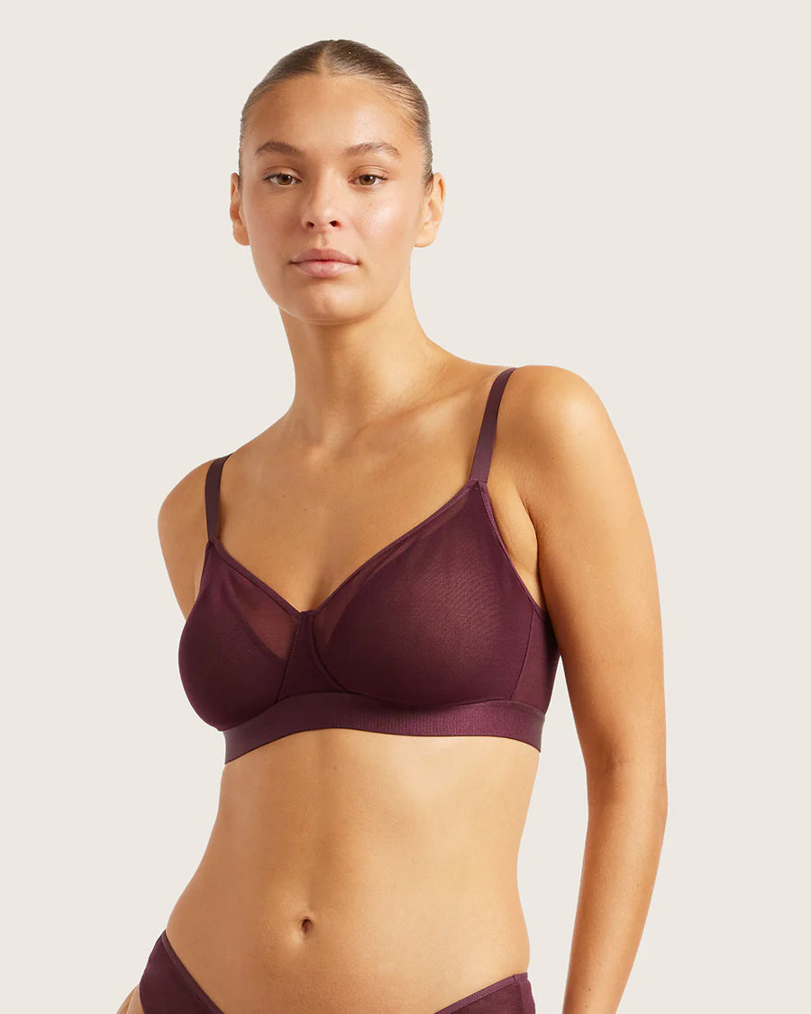Woman wearing a dark purple bra and underwear set on a plain background