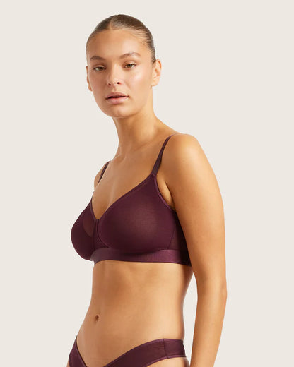 Woman wearing a dark purple bra and panties set on a light background