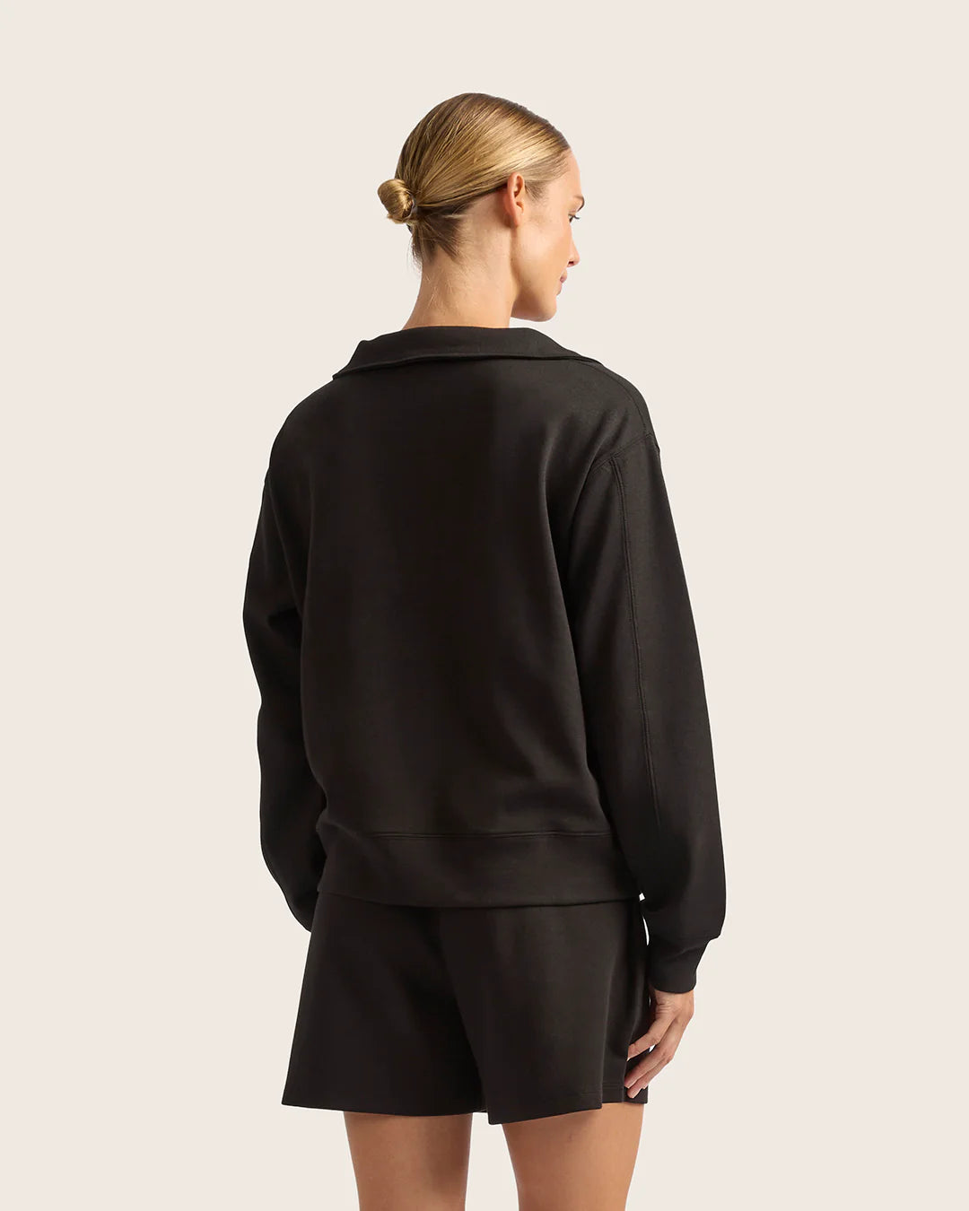Person wearing a black outfit on a light pink background
