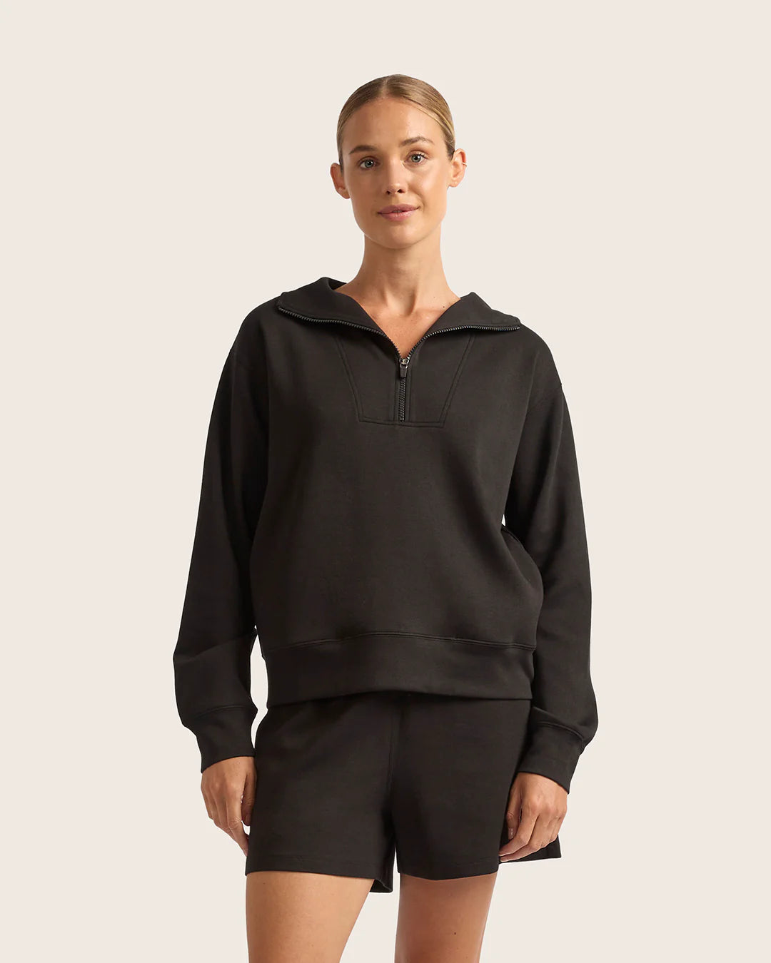 Woman wearing a black hoodie and shorts on a beige background