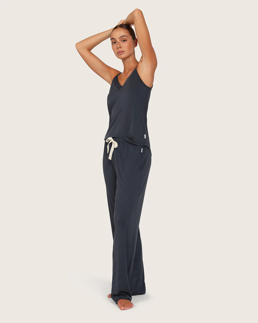 Woman wearing a dark blue jumpsuit with white drawstrings on a light beige background