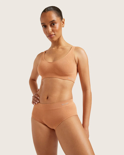 Woman wearing a beige sports bra and high-waisted leggings on a light background